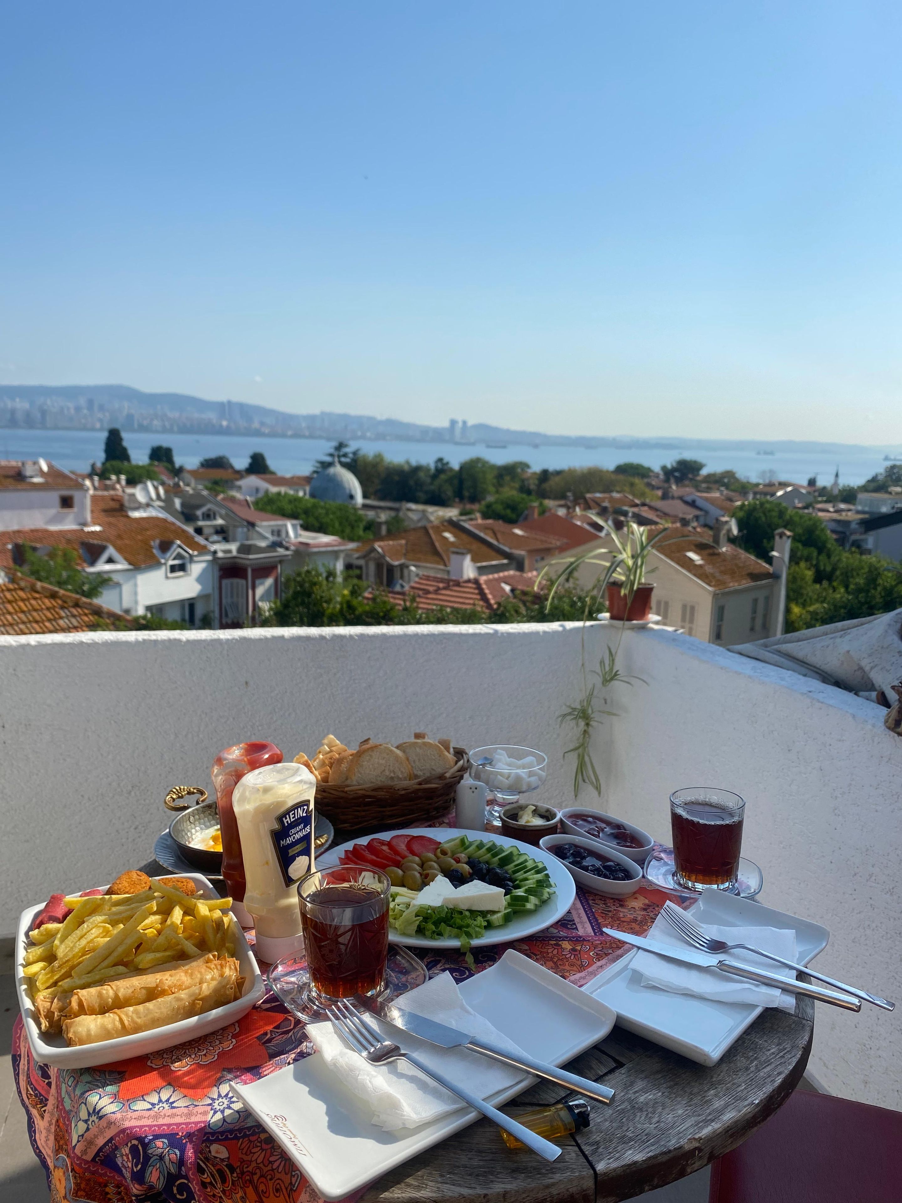 Una mesa preparada con comida y bebidas en un balcón con vistas a un paisaje urbano.