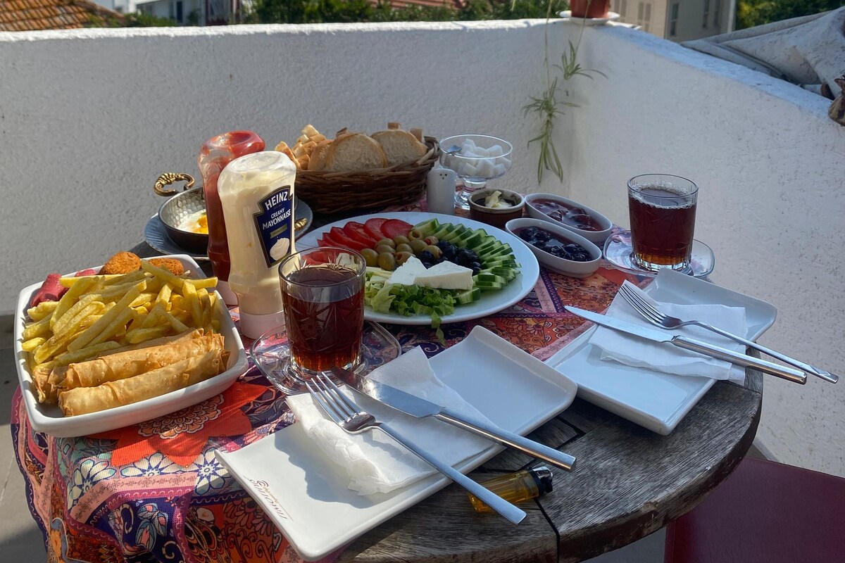 Una mesa preparada con comida y bebidas en un balcón con vistas a un paisaje urbano.
