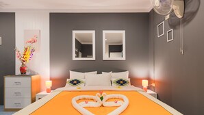 A hotel room with a bed, two bedside tables, a nightstand, a mirror, and a wall-mounted fan. - Rice Restaurant & Rooms (Karon)