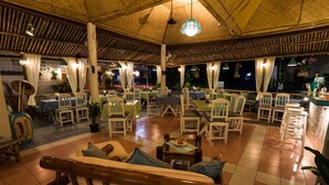 An indoor dining area with wooden furniture, a thatched roof, and hanging plants. - Rice Restaurant & Rooms (Karon)