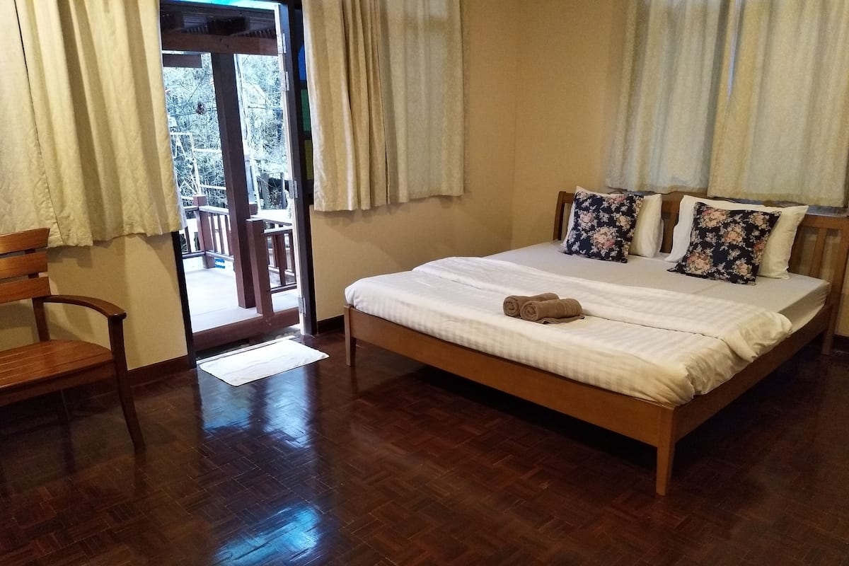 A bedroom with a wooden bed, a wooden chair, and a view through a glass door to an outdoor area.