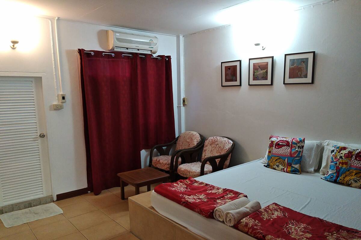 A bedroom with a bed, two chairs, a small table, and a red curtain.