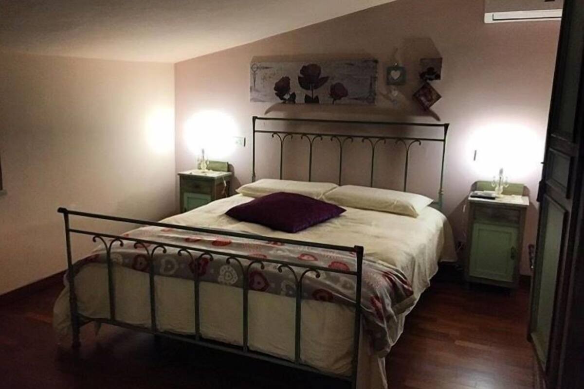 A bedroom with a metal bed frame, a single bed with a patterned bedspread, two bedside tables with lamps, and a wall-mounted artwork above the bed.