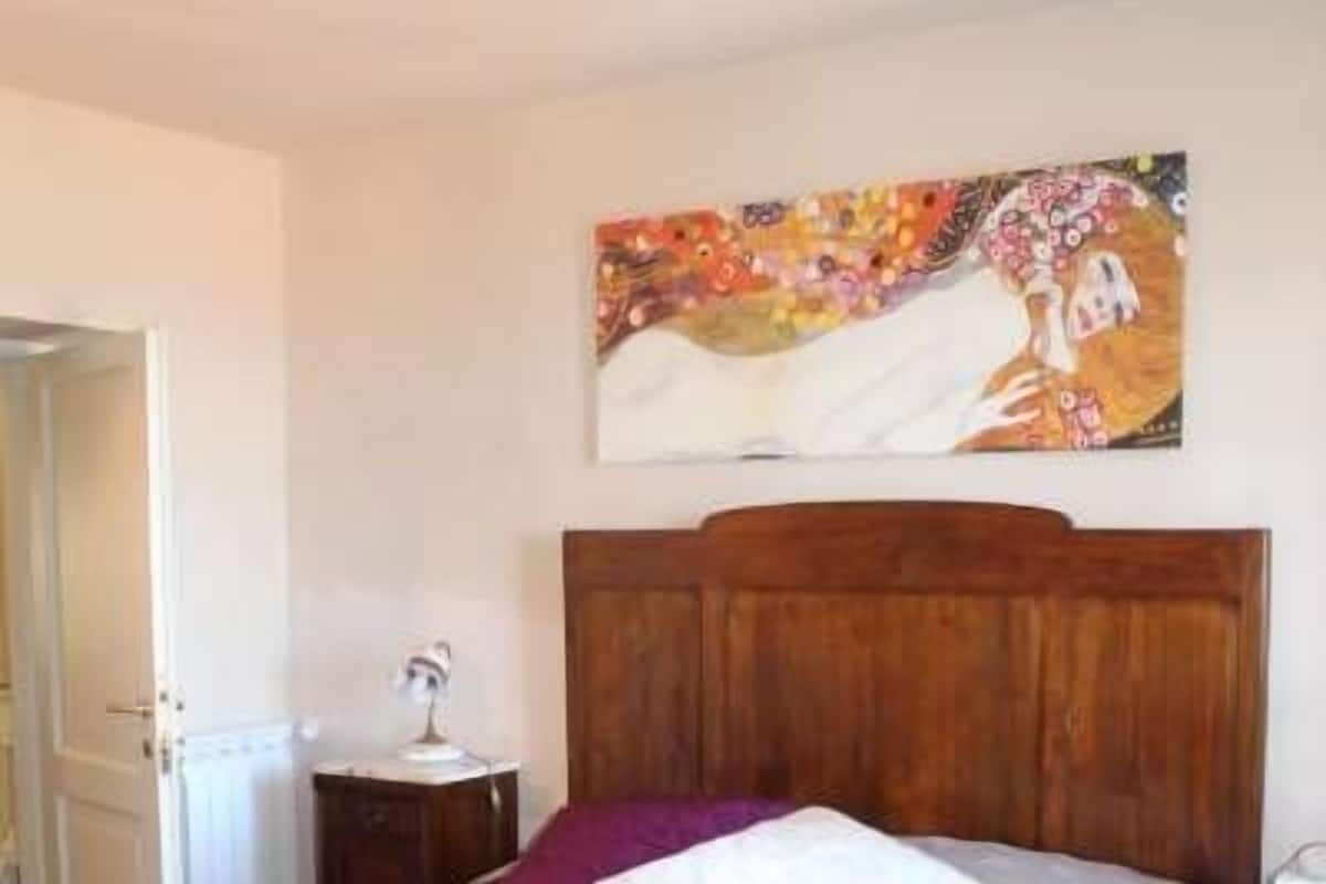 A bedroom with a wooden bed, a nightstand, a wall-mounted painting, and a door to the left.