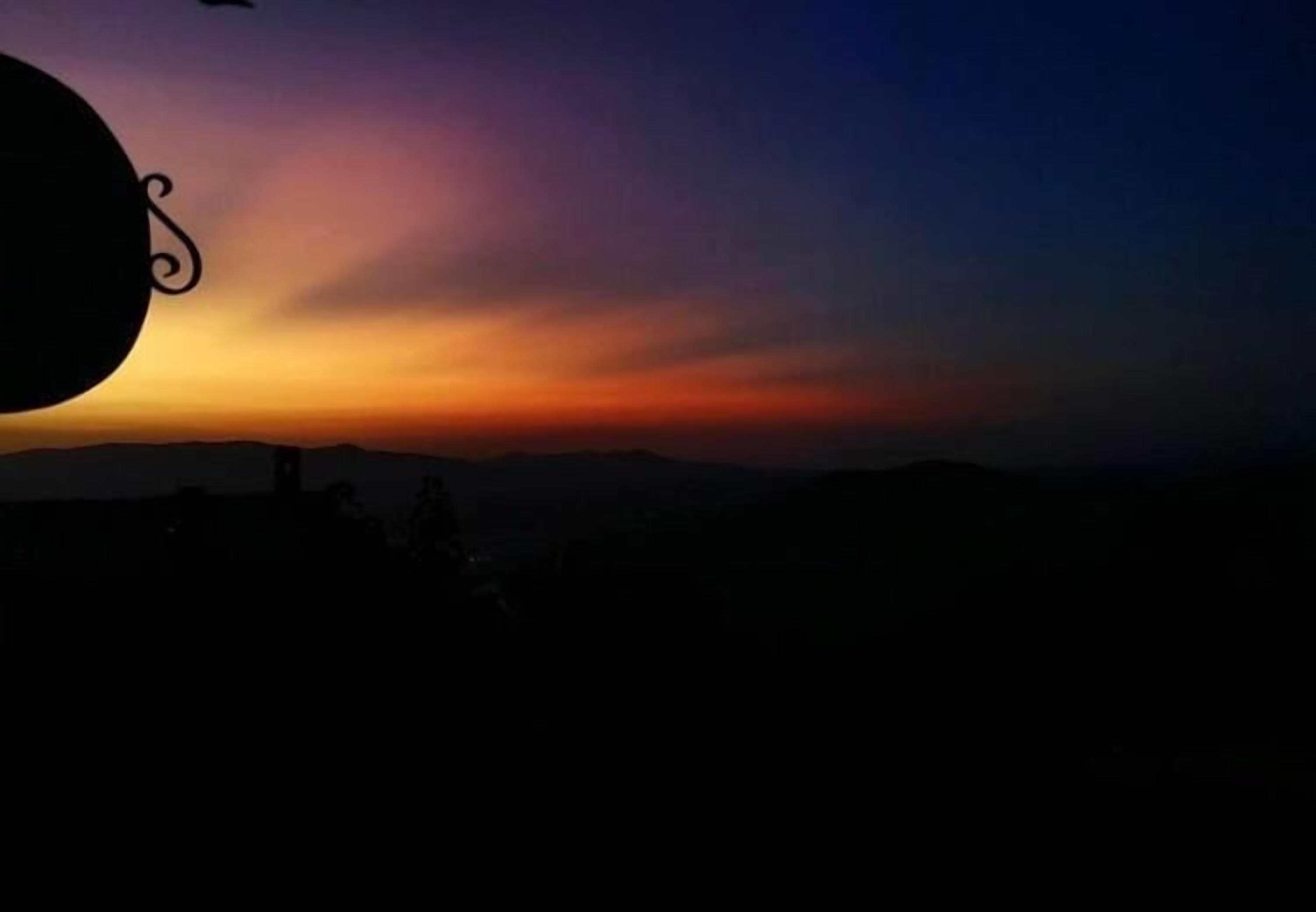 Vista al atardecer con siluetas de personas y una cadena montañosa.
