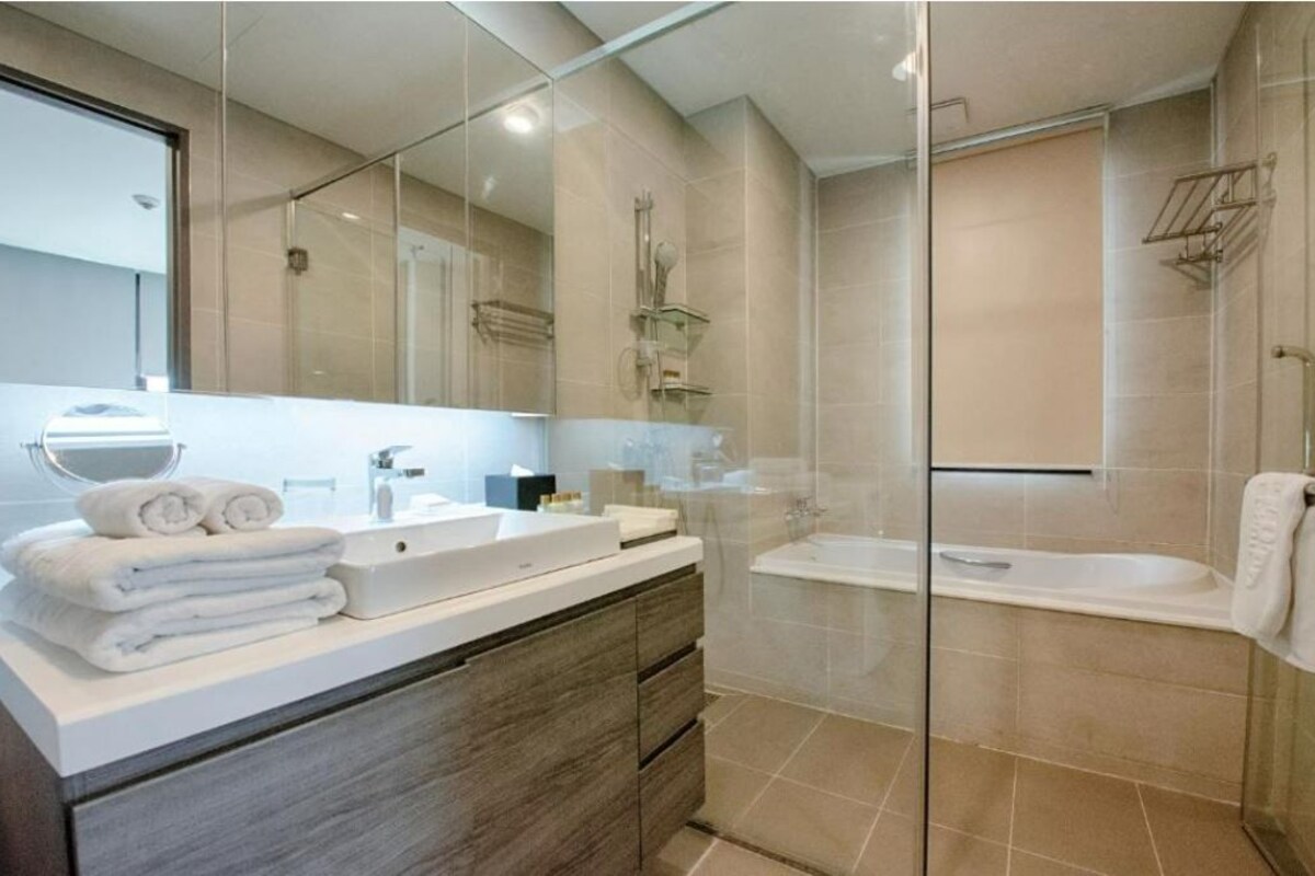 A modern bathroom with a glass shower enclosure, a bathtub, and a vanity with a mirror and towels.