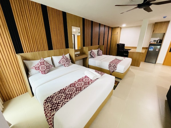 A hotel room with two beds, a wooden headboard, a desk, and a refrigerator.