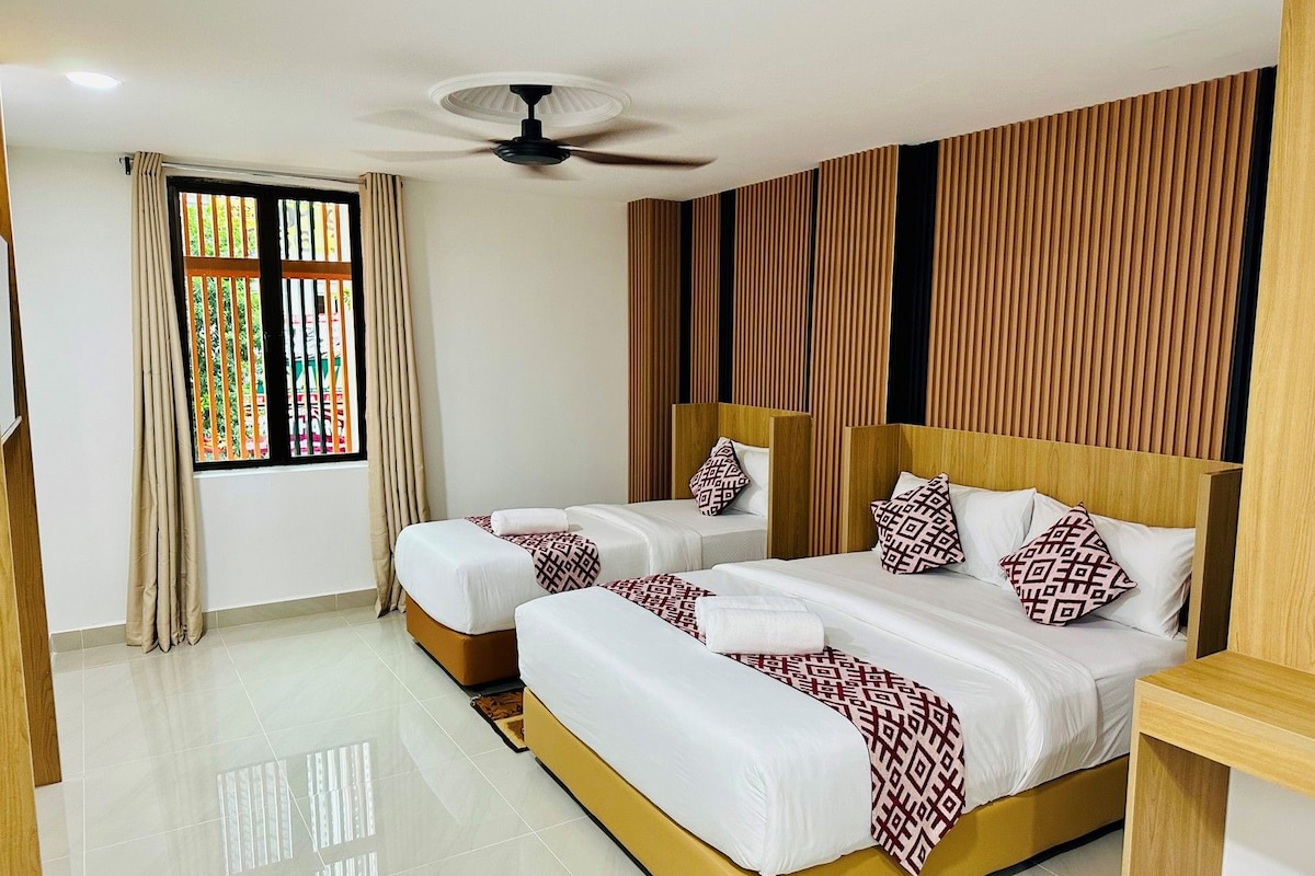 A hotel room with two beds, a ceiling fan, a window with curtains, and a wooden panel wall.