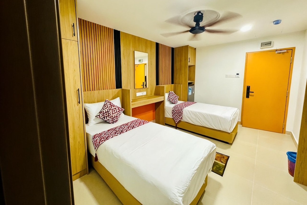 A hotel room with two single beds, a wooden wardrobe, a ceiling fan, and a door.
