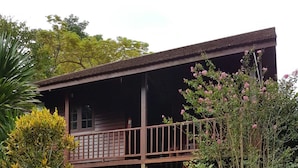 Una casa de madera con un porche, rodeada de abundante follaje y plantas con flores.