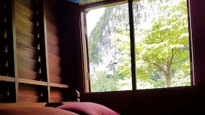 Una habitación con una cama, un ventanal con vistas a la vegetación y un estante de madera.