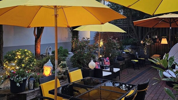 An outdoor patio with yellow umbrellas, wicker furniture, and potted plants. - Gästehaus Engelgasse (Herzogenaurach)