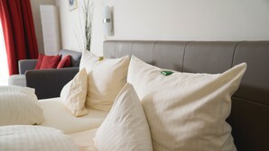 A neatly arranged hotel room with a bed, pillows, a sofa, and a red curtain. - Gästehaus Engelgasse (Herzogenaurach)
