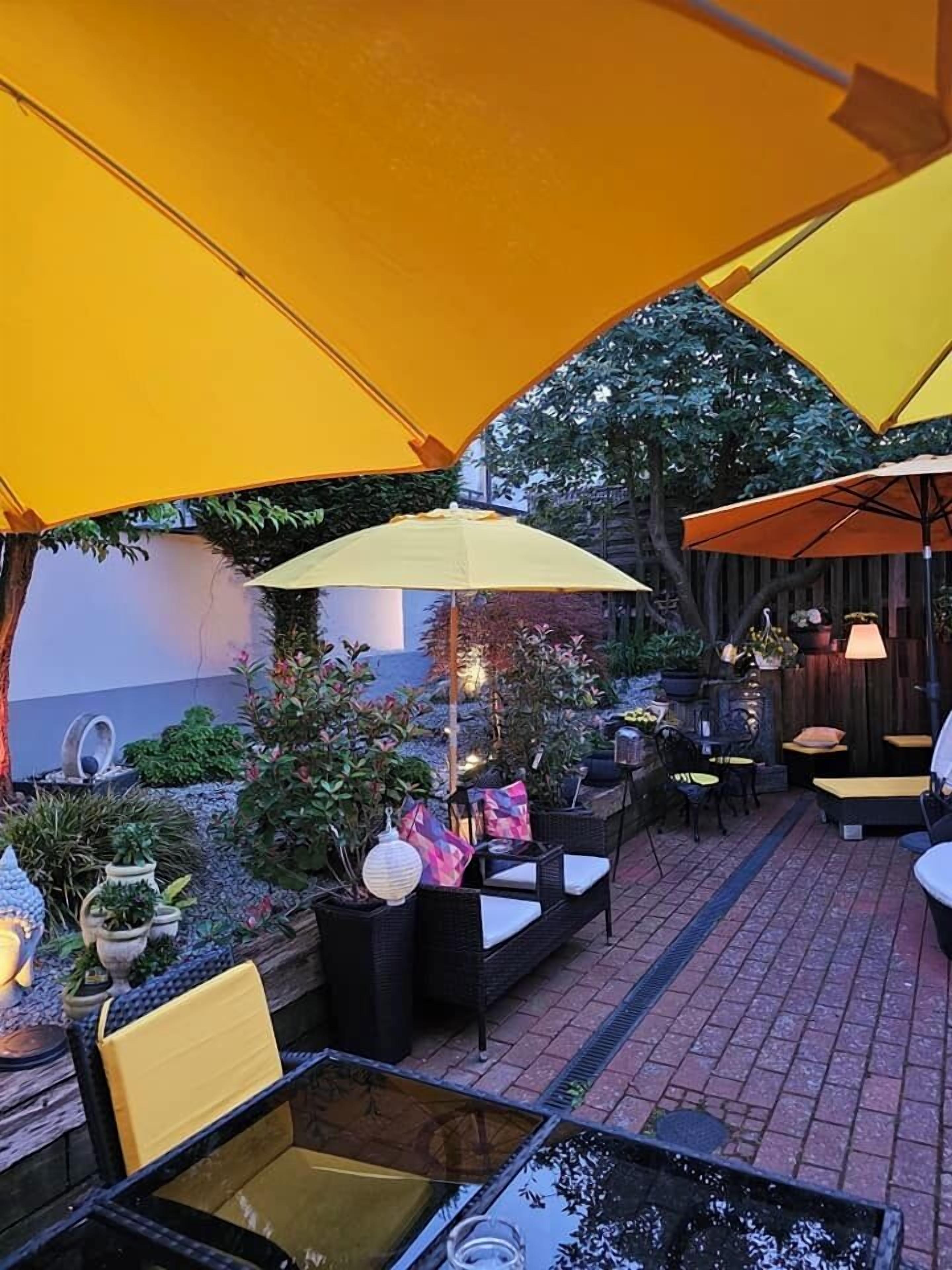 An outdoor seating area with yellow umbrellas, wicker furniture, and potted plants.
