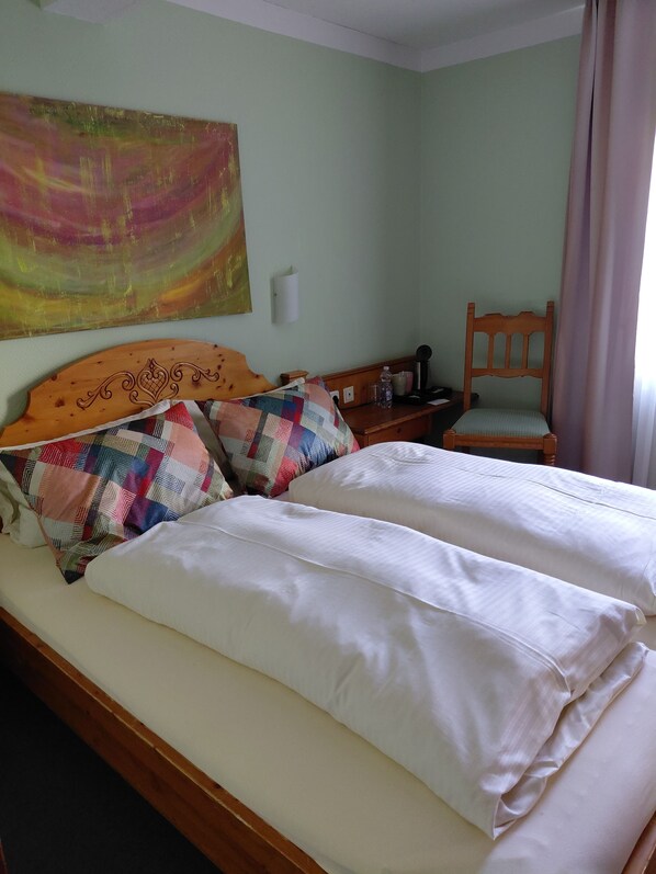 A bed with white linens, a wooden headboard, and a colorful pillow. - Gästehaus Engelgasse (Herzogenaurach)