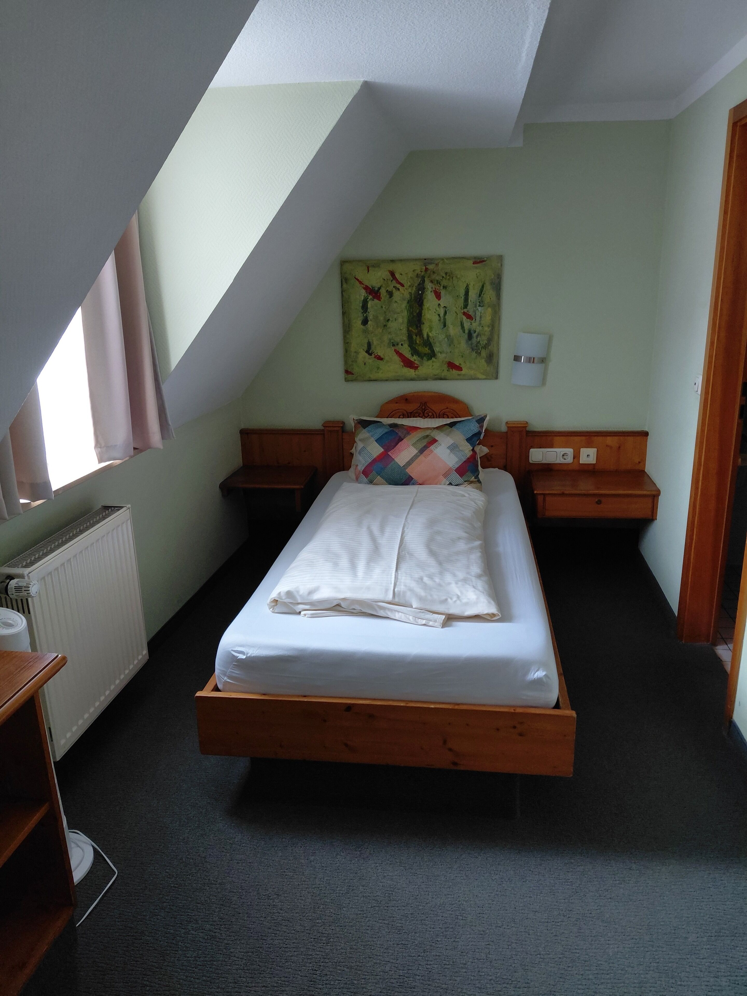 Ein Schlafzimmer mit einem Bett, einem Nachttisch, einer Wandlampe, einer Heizung und einem Fenster.
