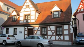 A traditional half-timbered building with a sloped roof, two cars parked in front, and a clear blue sky. - Gästehaus Engelgasse (Herzogenaurach)