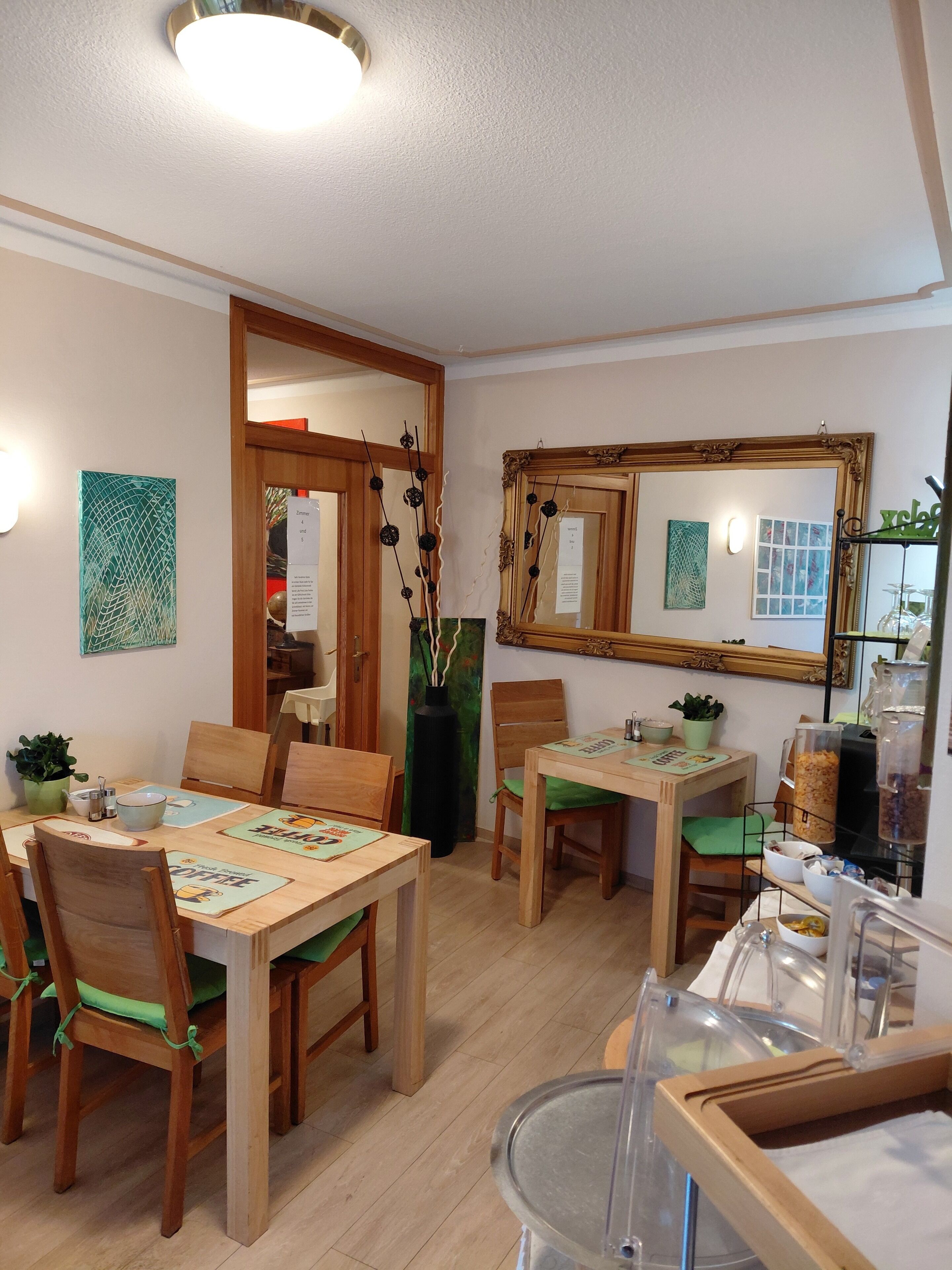 Un espace repas avec des tables et des chaises en bois, un grand miroir et un luminaire fixé au mur.