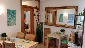 Un espace repas avec des tables et des chaises en bois, un grand miroir et un luminaire fixé au mur.