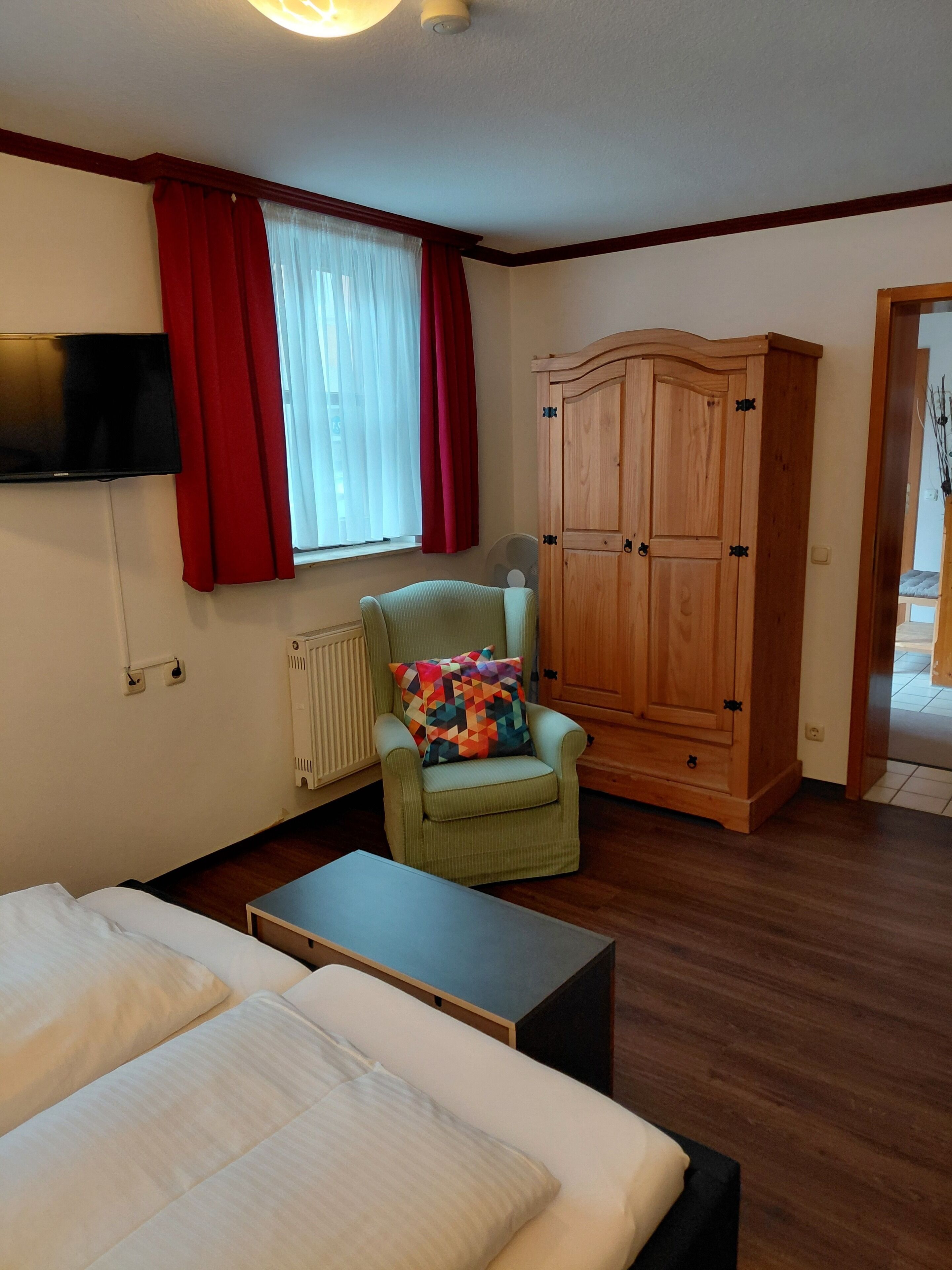 Una camera da letto con un letto, una sedia, una televisione, un armadio e una finestra con tende.