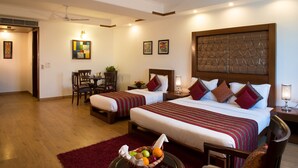 A hotel room with two beds, a dining area, and a ceiling fan. - Anila Hotel (New Delhi)