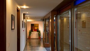 A hallway with framed pictures on the walls, potted plants, and a large abstract painting on the wall. - Anila Hotel (New Delhi)