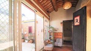 A cozy room with a sliding glass door leading to an outdoor area, a small table with chairs, and a wall-mounted shelf with decorative items. - O Share Sweet B&B (Jinning)