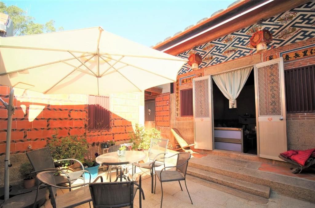 An outdoor seating area with a table and chairs, a large umbrella, and a traditional building with patterned walls and doors.
