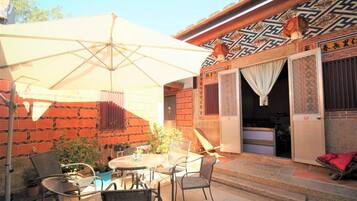 An outdoor seating area with a table and chairs, a large umbrella, and a traditional building with patterned walls and doors.