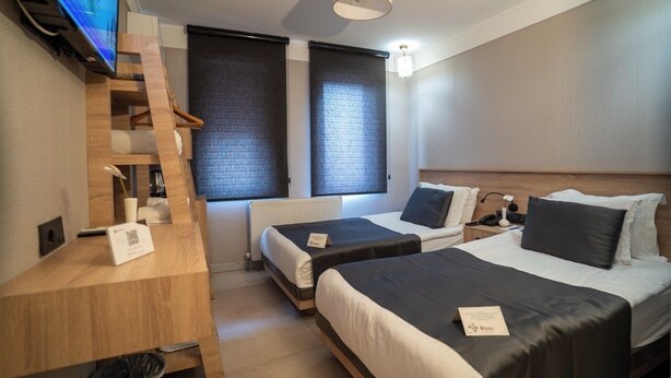 Habitación de hotel con dos camas, un escritorio de madera, televisor y ventana con persiana.
