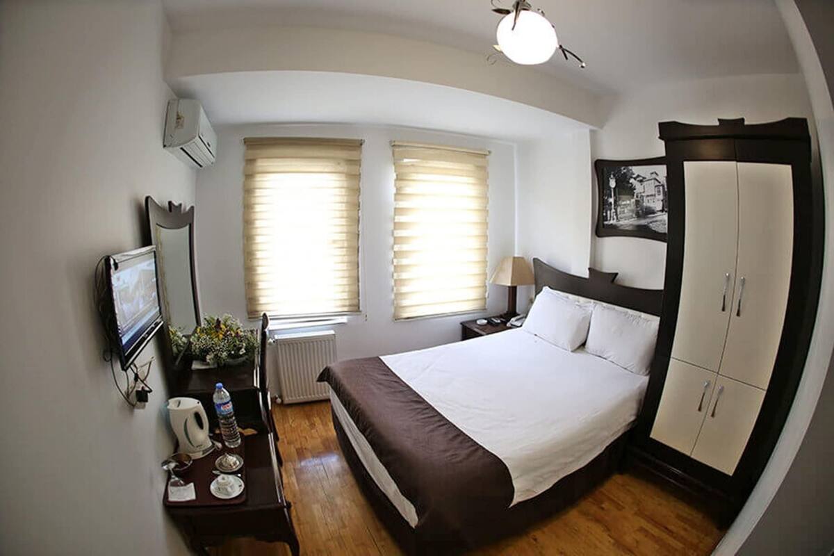 A hotel room with a bed, bedside table, lamp, wardrobe, and a television.