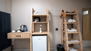 Ein kompaktes Hotelzimmer mit Schreibtisch aus Holz, kleinem Kühlschrank, Ablagefach für Toilettenartikel, Handtuchhalter und Papierkorb.