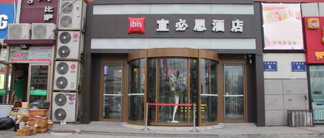 A hotel entrance with a curved glass door, a red ribbon barrier, and a sign with Chinese characters.