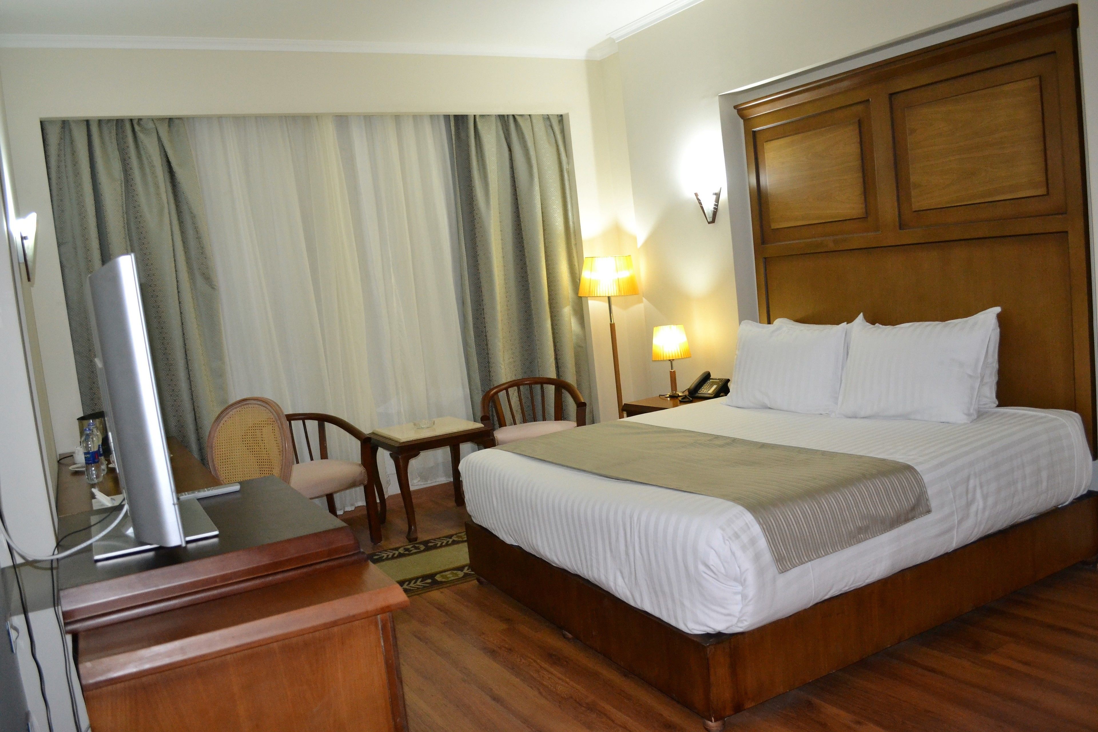 A hotel room with a wooden bed, a desk with a lamp, and a television on a stand.