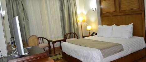 A hotel room with a wooden bed, a desk with a lamp, and a television on a stand.