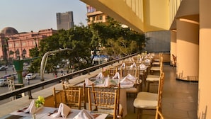 En restaurang med bord uppställda för servering, uteservering och utsikt över en stadsbild, inklusive en framträdande byggnad med en kupol.