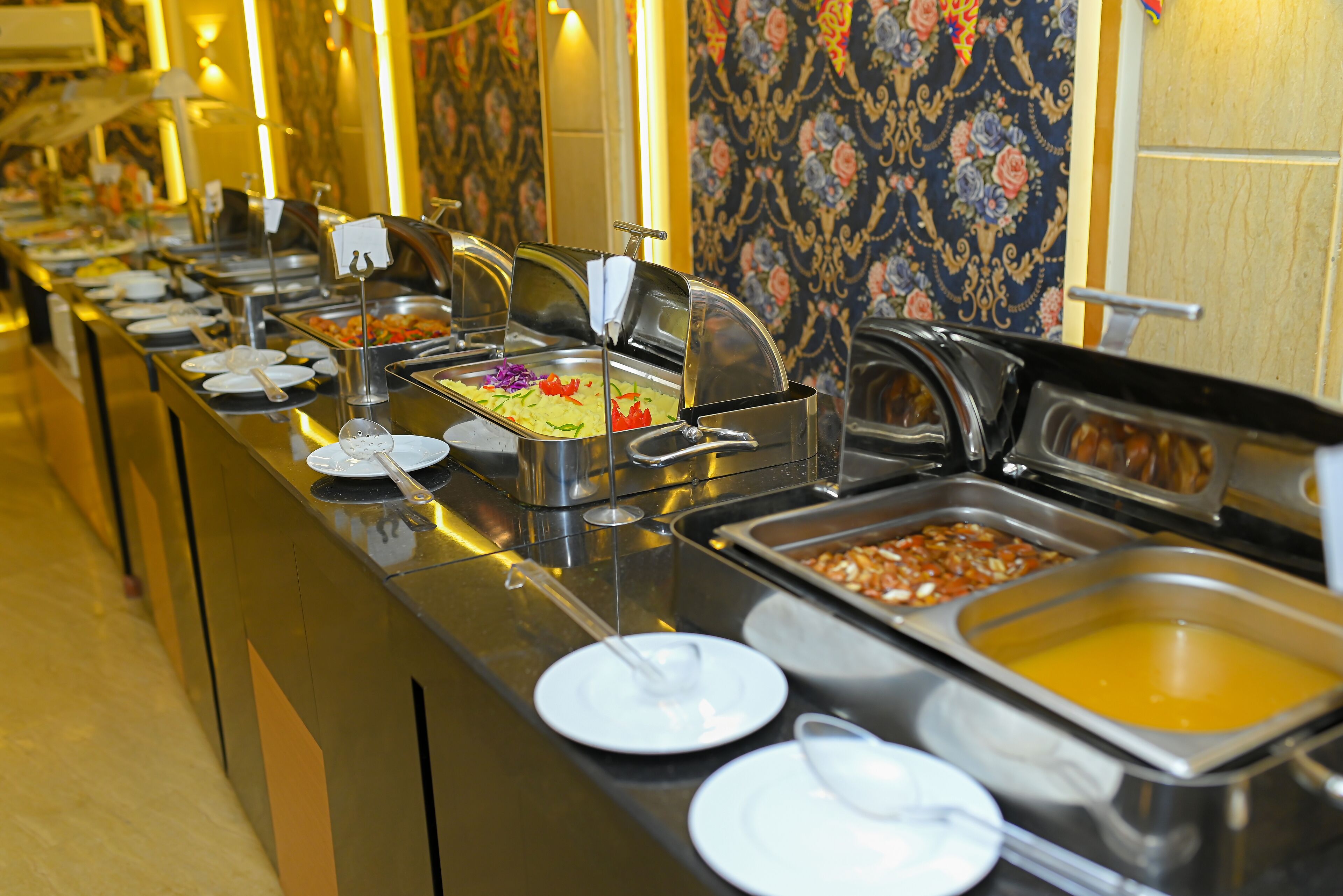 Una barra de buffet con diferentes estaciones de comida, cada una con un recipiente cubierto y una cuchara.