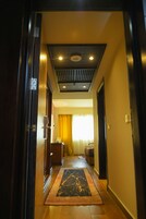Un pasillo con suelo de madera, alfombra estampada, techo con luces empotradas y una ventana con cortinas amarillas.