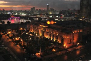 A large, historic building with a dome and arched windows, surrounded by a well-lit plaza and a river.