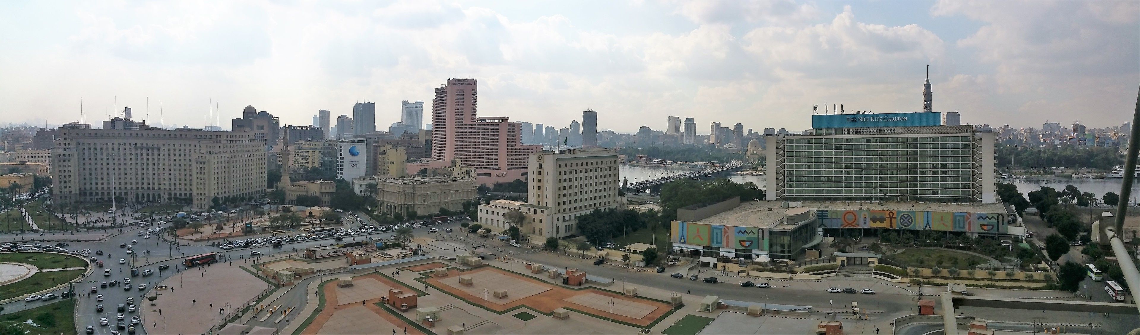 A cityscape with a prominent hotel named "The Nile Ritz Carlton" featuring a modern design and a view of the river.