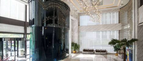 A modern lobby with a central cylindrical structure, large windows, and a chandelier.