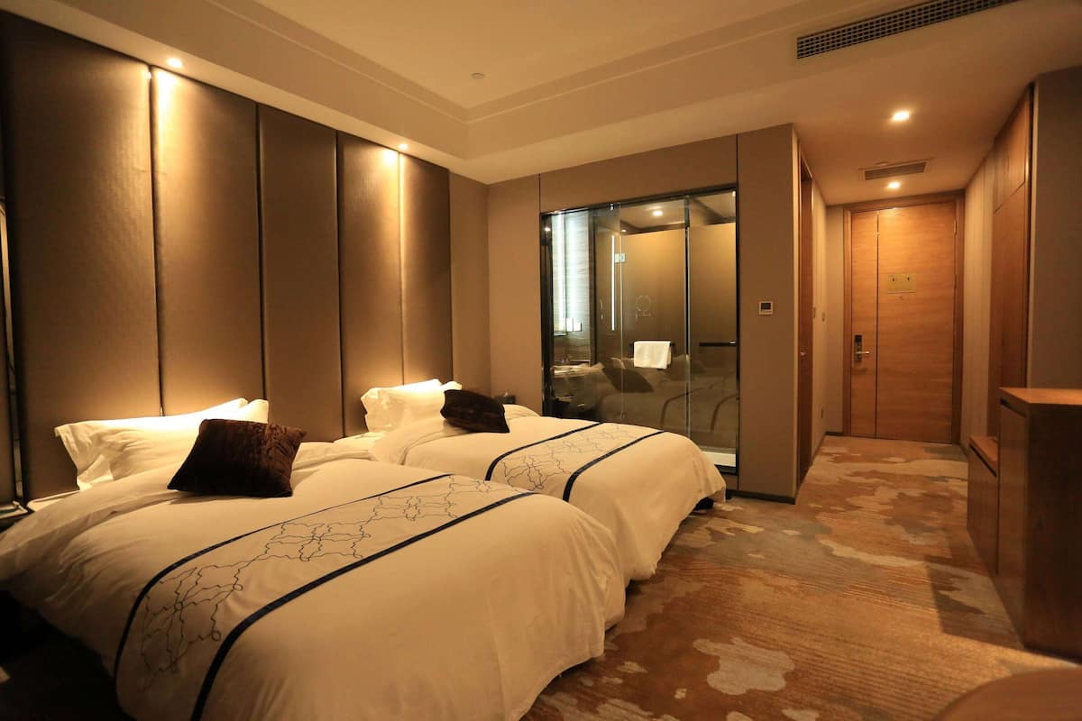 Habitación de hotel con dos camas, cabina de ducha de vidrio y armario de madera.