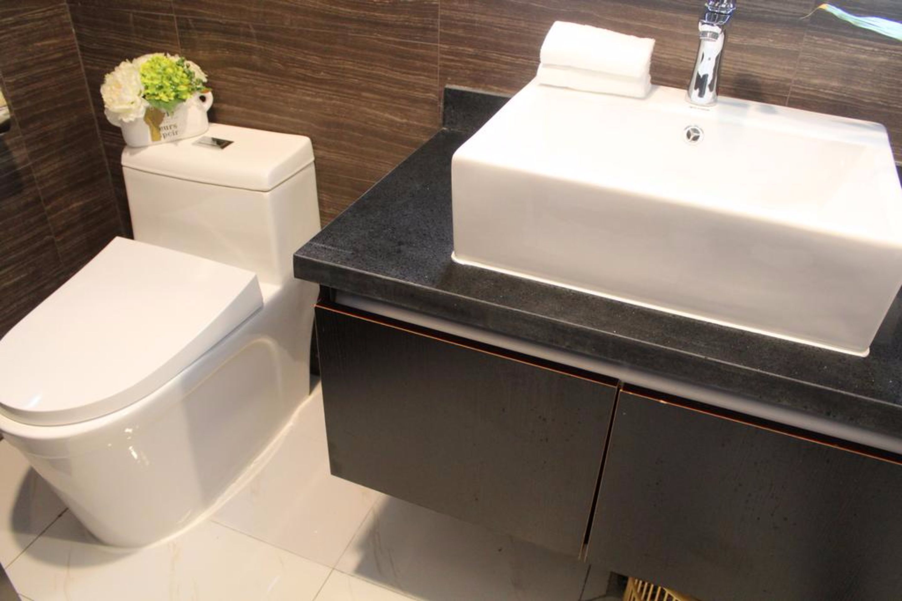 Un baño moderno con inodoro blanco, encimera negra y lavabo blanco.