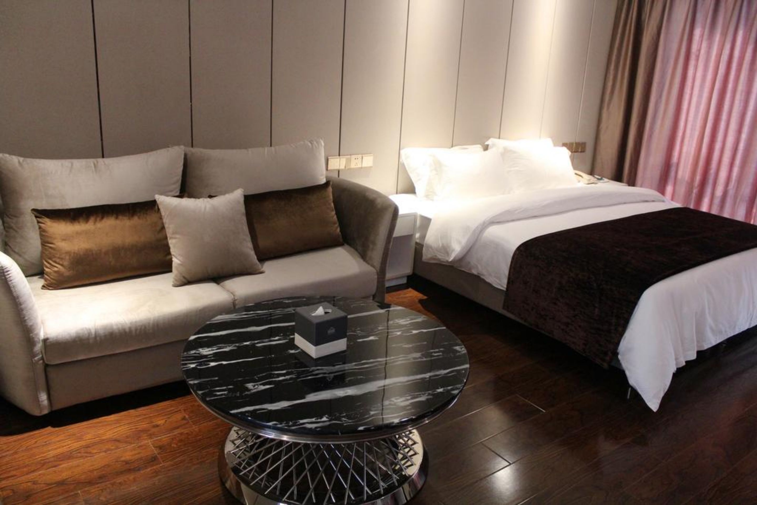 Quarto de hotel moderno com sofá, cama e mesa de centro redonda.