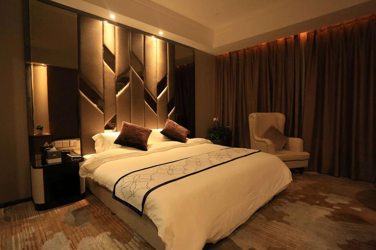 Una habitación de hotel moderna con una cama grande, una mesita de noche, una silla y un espejo amplio.