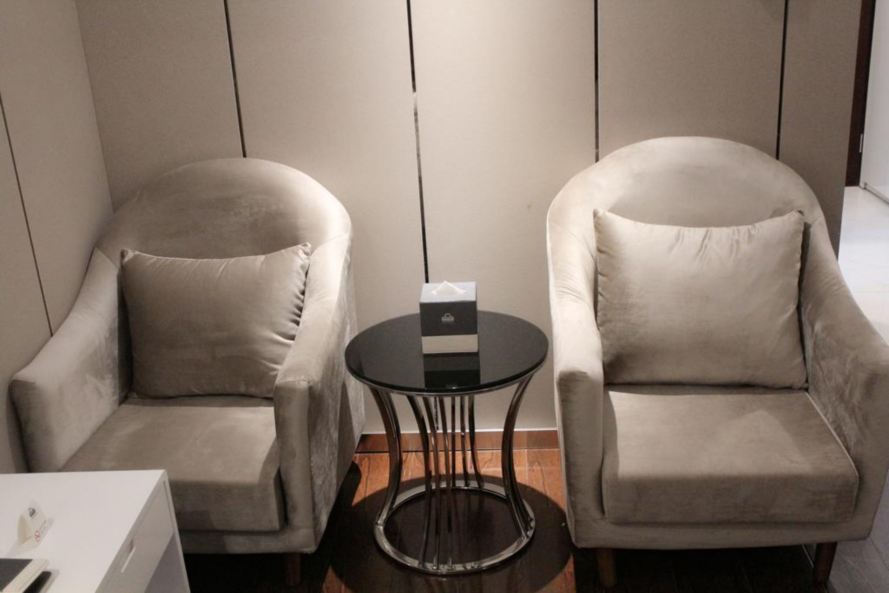 Deux fauteuils, une petite table ronde placée entre eux, une boîte sur la table et un meuble blanc sur le côté gauche.