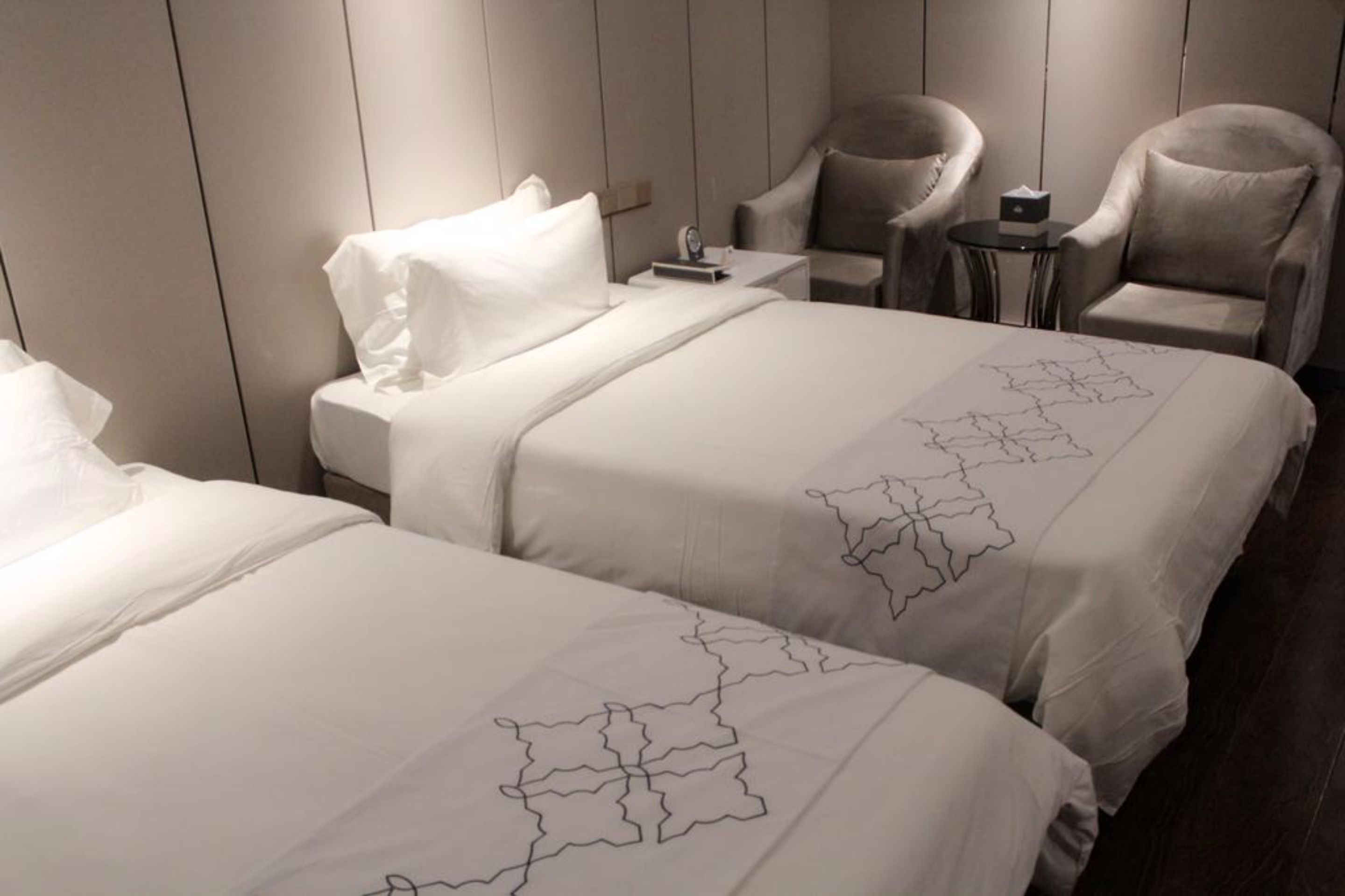 A hotel room with two beds, a small table, and two armchairs.