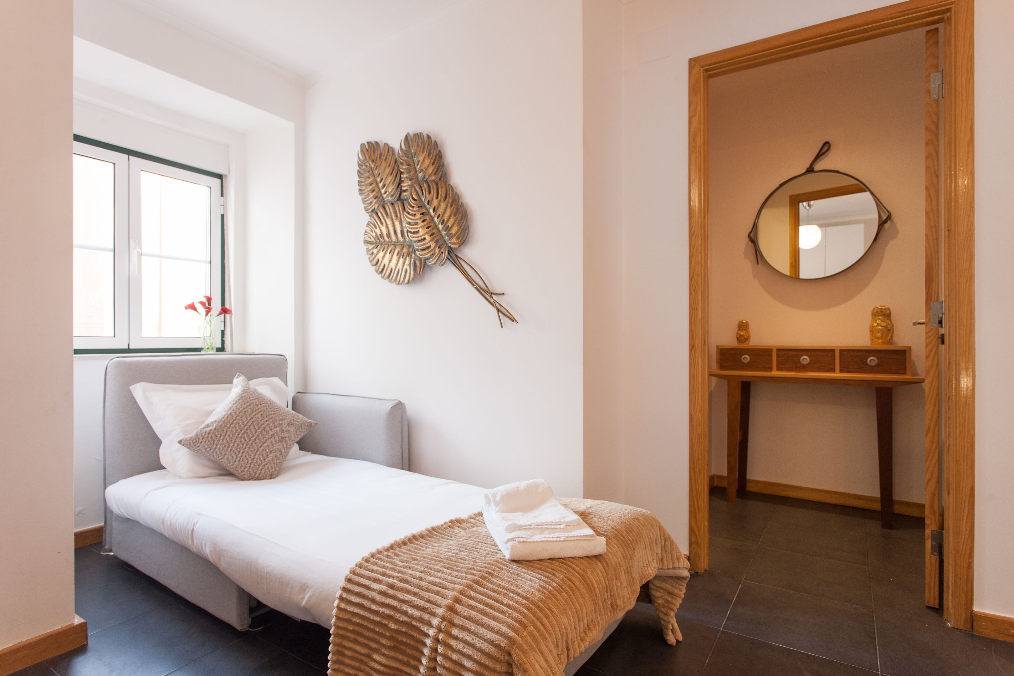 Een slaapkamer met een bed, nachtkastje, spiegel en een decoratief blad aan de muur.