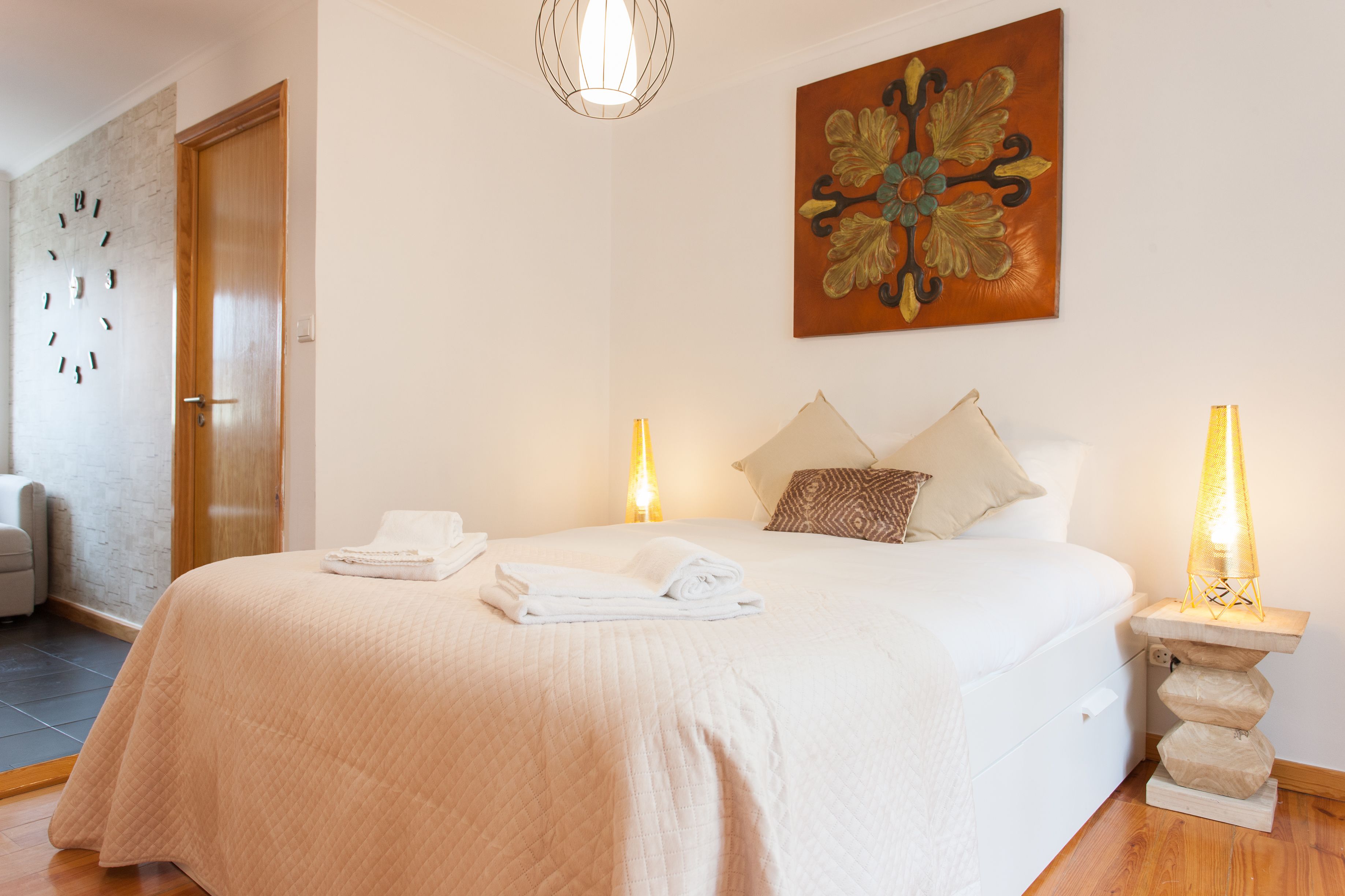 A neatly made bed with a quilted blanket, two bedside lamps, and a decorative wall piece.