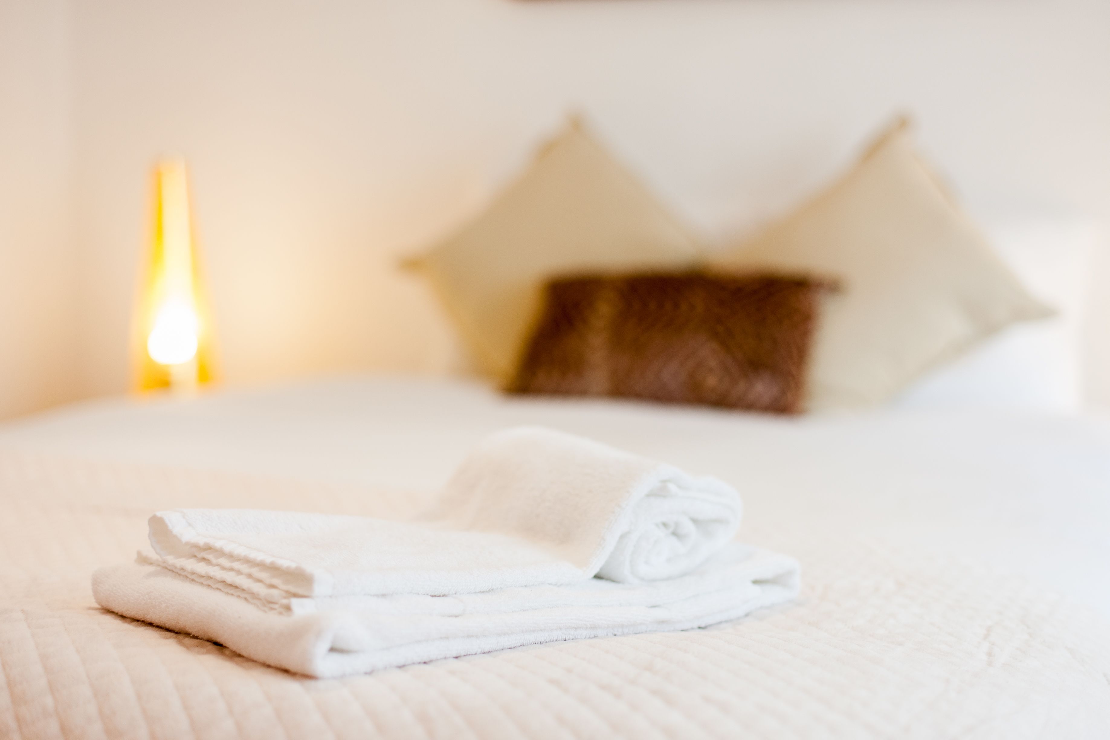 A neatly made bed with a folded white towel in the foreground and a pillow in the background.